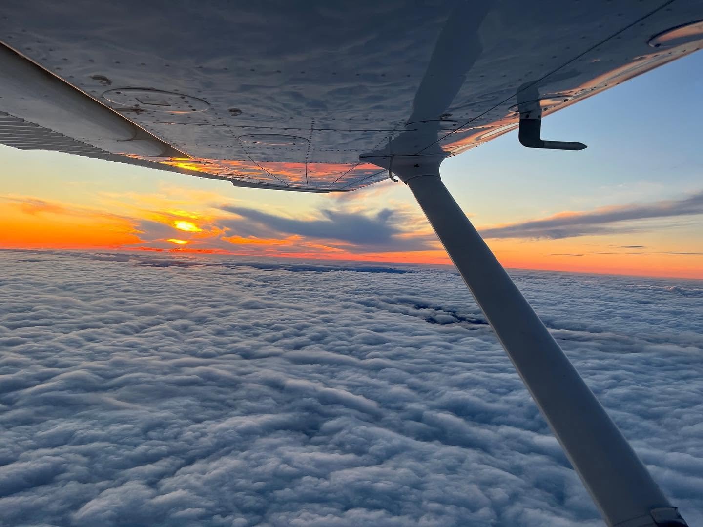 View from the wing of a training aircraft flying above a cloud deck at sunset